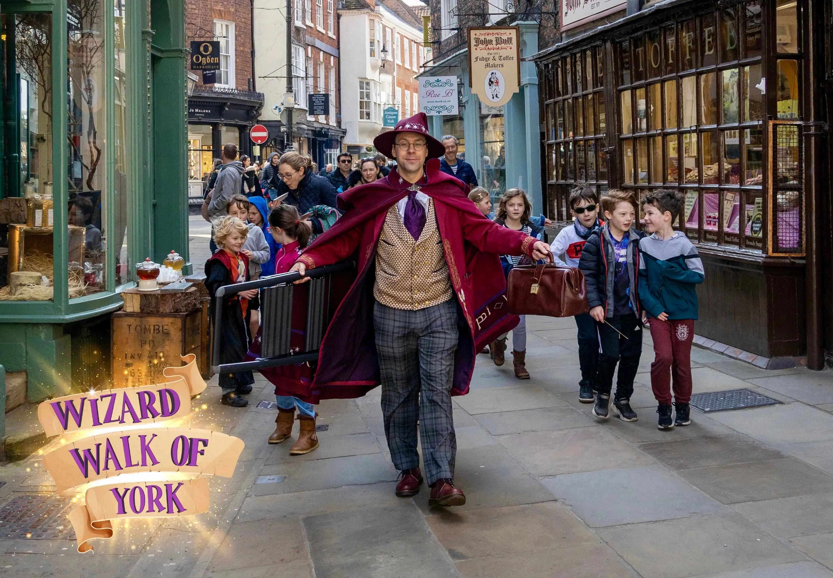 Wizard of York with his cape wide striding down the Shambles in York followed by lots of children.